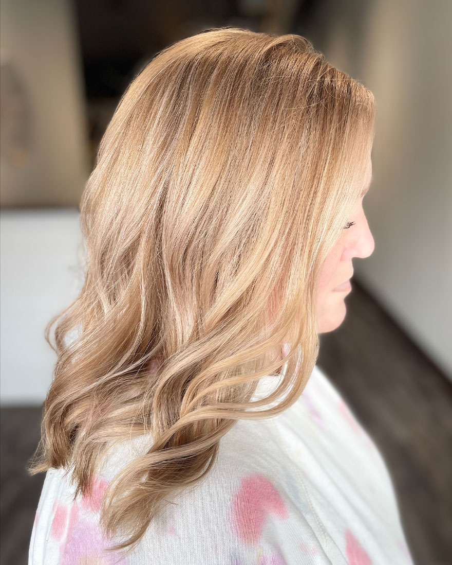 Woman with shoulder-length, light blond, wavy hair with honey-blond highlights at Hygge Hair Studio.