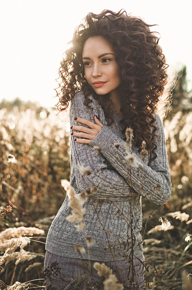 Woman with long, curly, brown hair outside in the sunshine.