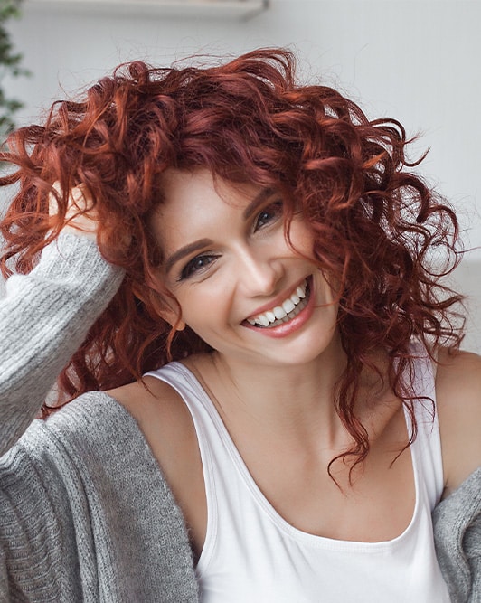 Woman with long, curly, red hair is smiling.
